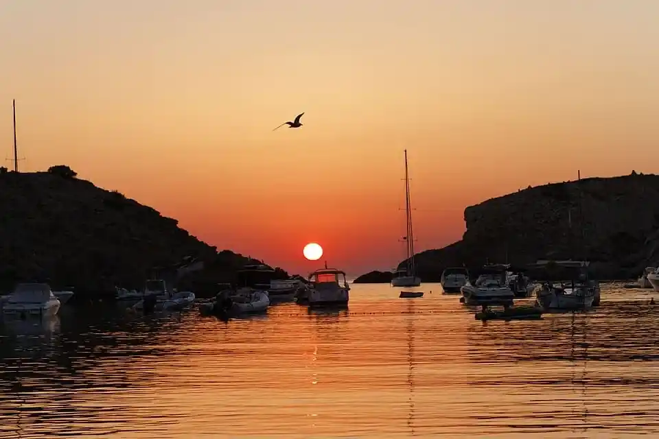 Puesta de sol en Cala Vadella con barcos fondeados y el reflejo del sol en la costa oeste de Ibiza