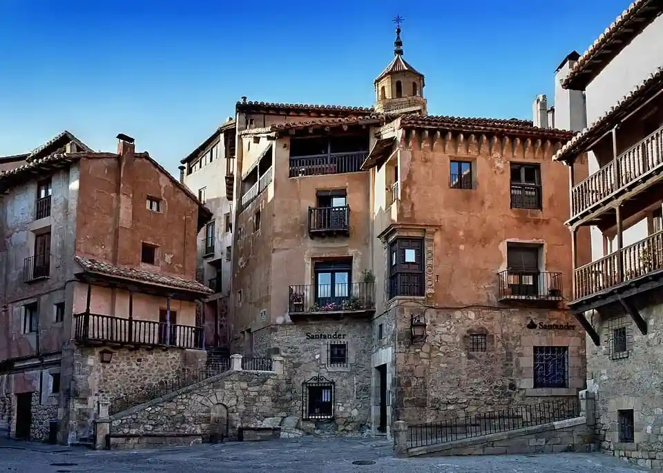 Casas tradicionales de yeso rojo y balcones de madera en la Plaza Mayor de Albarracín con la torre de la catedral al fondo, Teruel.