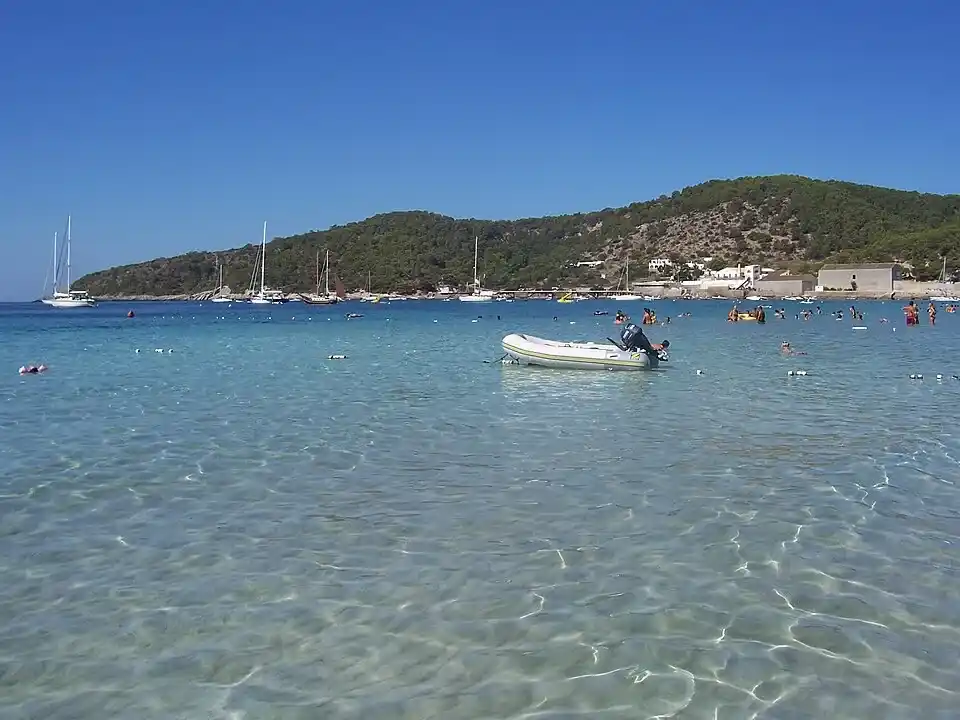 Aguas cristalinas y transparentes en la playa de Ses Salines en Ibiza con bañistas y lanchas fondeadas