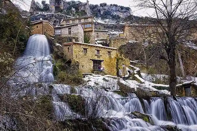 Cascada de Orbaneja del Castillo con efecto seda fluyendo entre casas tradicionales y laderas cubiertas de nieve en Burgos.