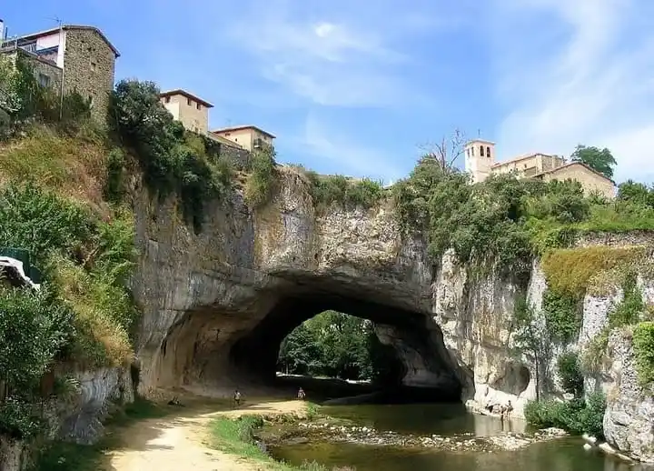 Monumento natural de roca y arco del puente de Puentedey sobre el río Nela con el pueblo y la iglesia en lo alto, Burgos.
