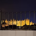Catedral de Málaga iluminada de noche vista a través de una barandilla, con su torre dorada reflejando la luz nocturna contra el cielo azul. Un imprescindible que ver en Málaga en 2 días, esta joya arquitectónica combina historia, arte y belleza en el corazón de la ciudad.