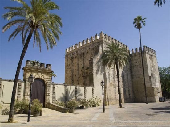 Entrada principal del Alcázar de Jerez de la Frontera con su torre fortificada, murallas almenadas y palmeras bajo cielo azul