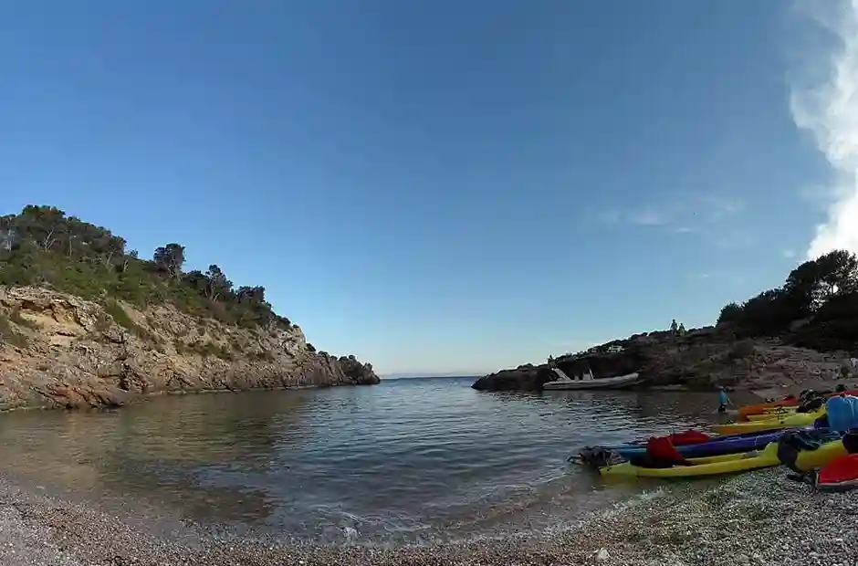 Cala Olivera, una pequeña cala de Ibiza con aguas cristalinas, orilla de piedras y kayaks descansando en la orilla