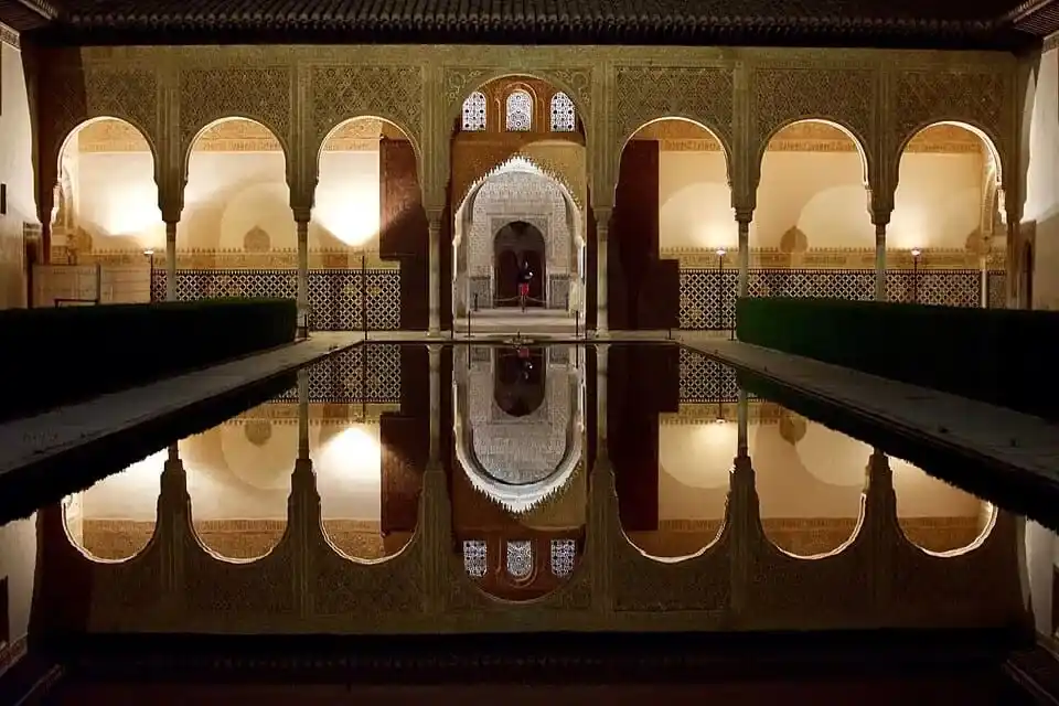 Reflejo nocturno de la galería de arcos iluminados del Patio de los Arrayanes en los Palacios Nazaríes de la Alhambra.